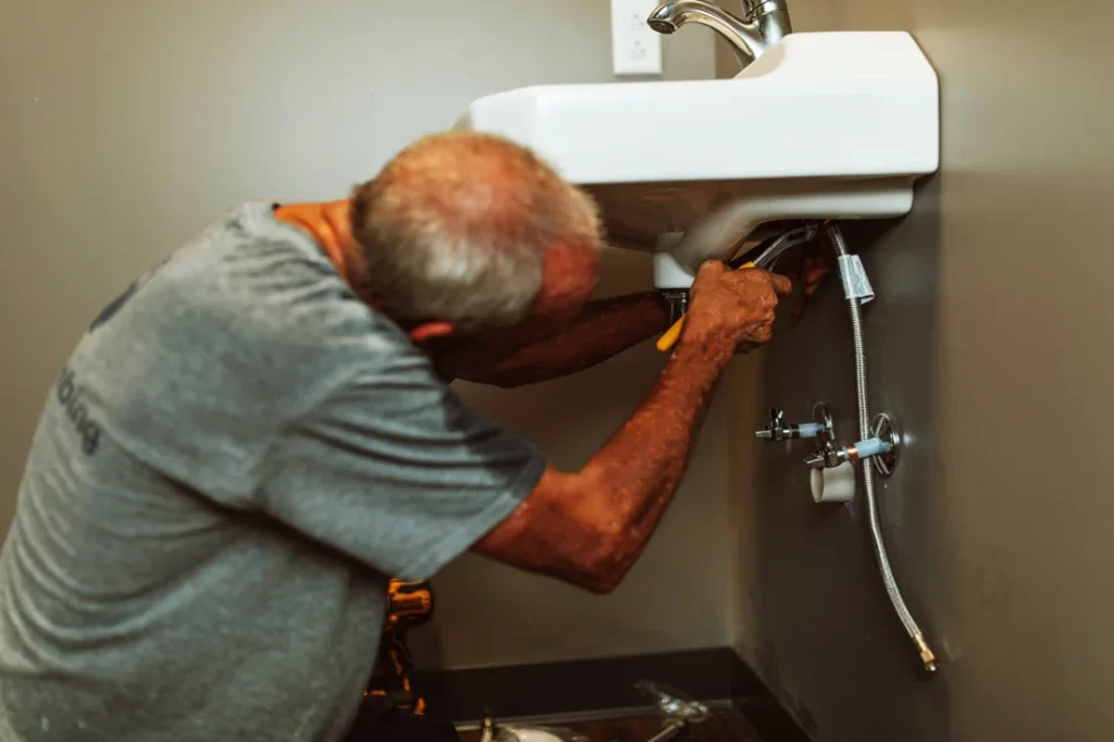 Licensed plumber from B & C Plumbing performing drain cleaning under a sink in Huntsville, Alabama